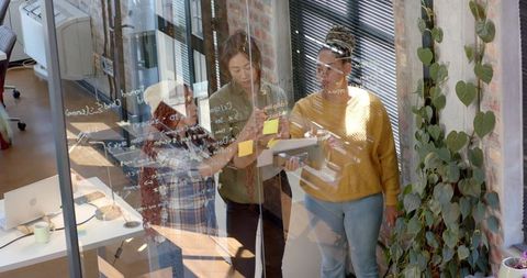 Team of Diverse Women Collaborating Around Glass in Modern Office