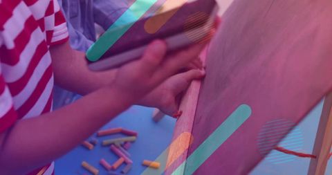 Two children drawing at easel using tablet and colorful chalk for collaborative play