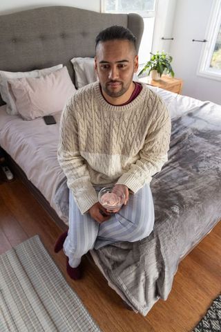 Man sitting on bed holding dessert bowl in cozy neutral bedroom with morning light