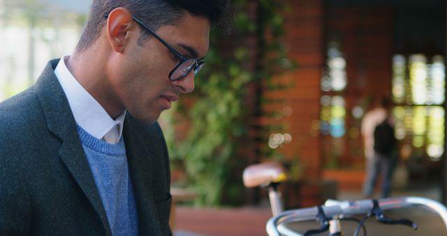 Young businessman wearing glasses in a modern city environment, standing next to a bicycle. Ideal for illustrating urban professionals, sustainable transport, or modern lifestyle. Could be used for business publications, websites promoting green transportation, or advertising modern workspace concepts.