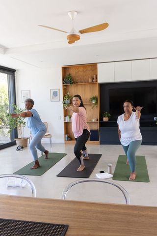 African american women practicing yoga together at home doing warrior pose on mats