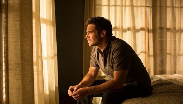 Man sitting on bed gazing through sunlit curtains during quiet contemplative moment