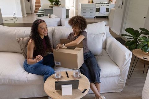 African american friends unpacking delivery box on sofa, smiling unboxing moment at home