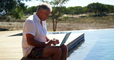 Middle-Aged Man Remote Working by Poolside on Sunny Day