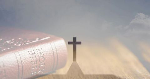 Leather holy bible with cross silhouette casting long shadow on wooden tabletop for faith
