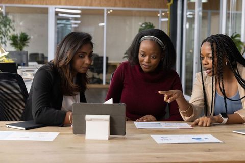 Diverse female team collaborating over tablet and charts in modern open-plan office