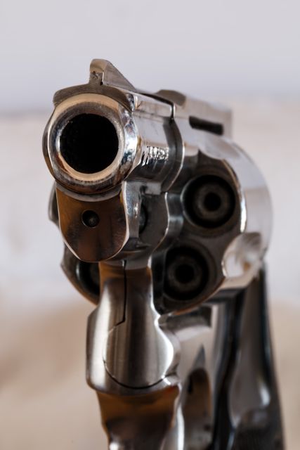 This close-up image of a revolver barrel aimed directly at the camera lens emphasizes the seriousness and danger associated with firearms. Suitable for use in materials related to crime prevention, personal defense, law enforcement, or discussions on gun control. Can also be used in dramatic storytelling or illustration of confrontation in media.