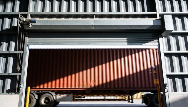 Red cargo container sliding through industrial loading bay rollup door with trailer wheels
