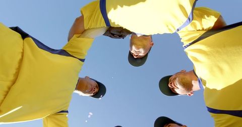 Male baseball team huddling under blue sky wearing yellow jerseys for pregame unity