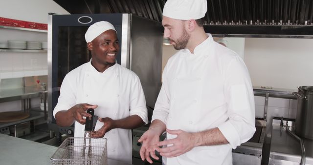 This image depicts two chefs in a commercial kitchen, collaborating and communicating. Can be used for concepts related to professional cooking, teamwork, culinary education, restaurant industry, and diversity in the workplace.