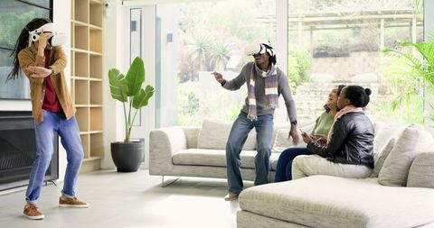 Diverse friends playing virtual reality and laughing in bright modern living room scene