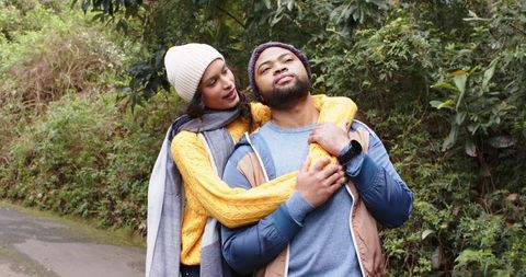 African american couple embracing on leafy trail wearing knit beanies and smartwatch