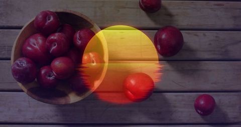 Vibrant red plums in wooden bowl with artistic sun overlay