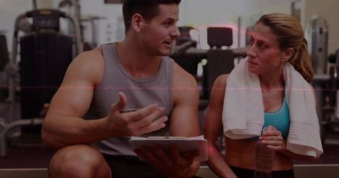 Personal trainer consulting female client after strength workout holding tablet water bottle in gym