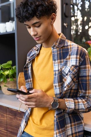 Young Man in Plaid Shirt Using Smartphone in Cozy Kitchen