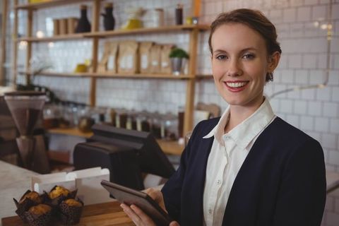 Young Barista at Cafe Counter Holding Tablet Near Muffins