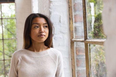 Contemplating woman by window admiring lush outdoor greenery