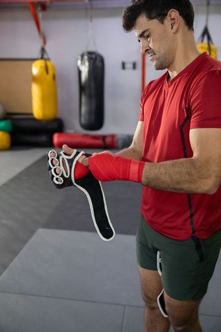 Boxer fastening fingerless glove while wrapping hands in boxing gym training