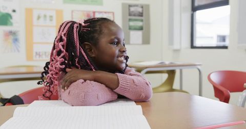 Joyful Child Smiling at School Desk with Pink Sweater and Notebook