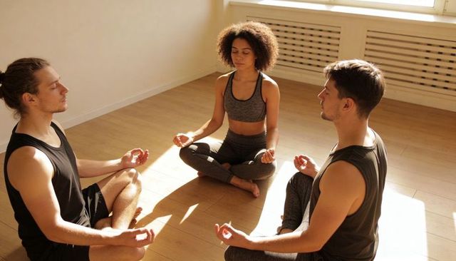 Three adults meditating in sunlit studio practicing Gyan mudra for calm and wellness