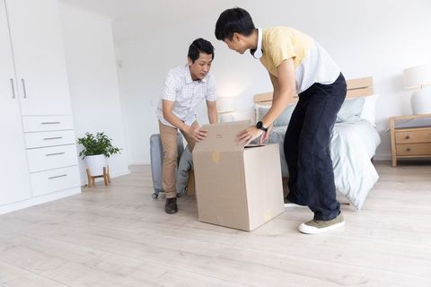 Two asian roommates unpacking cardboard box during move in bright minimalist bedroom