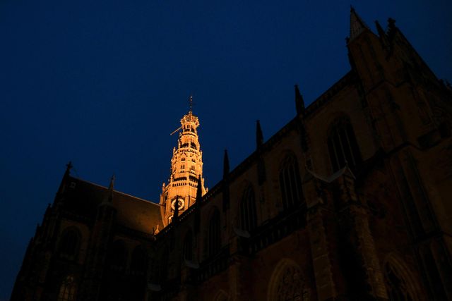 Picture of a Gothic cathedral with a prominent clock tower, beautifully illuminated against a deep blue night sky. Perfect for use in travel brochures, cultural heritage articles, postcards, and as a visual in content discussing historical architecture and landmarks.