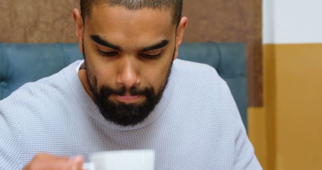 Man with beard drinking coffee in cafe. Ideal for use in articles about coffee culture, relaxation, leisure activities, and indoor lifestyles. Suitable for promoting cafes and coffee-related products.