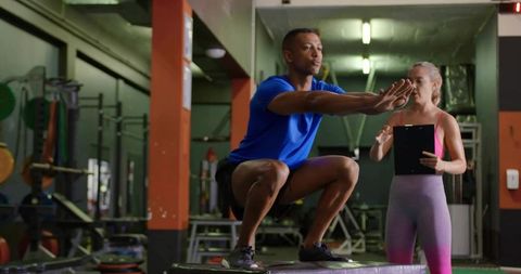 Male athlete performing deep squat on plyo box while trainer evaluating technique