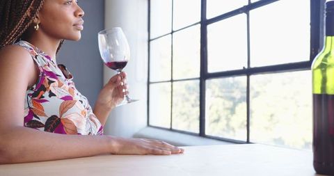 Woman Savoring Red Wine Near Sunlit Window, Relaxation at Home