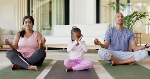 Family meditating together on yoga mats at home parents and daughter practicing mindfulness