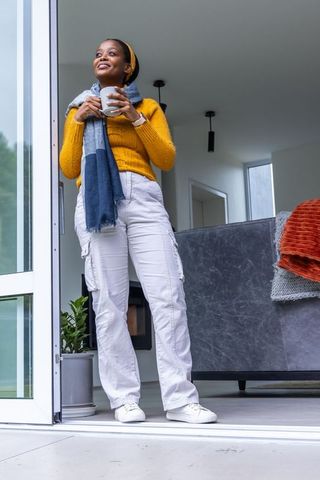 Serene african american woman standing at glass door holding mug in cozy modern home