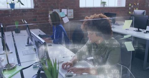 Typing developer working at keyboard in modern open-plan office with plexiglass dividers