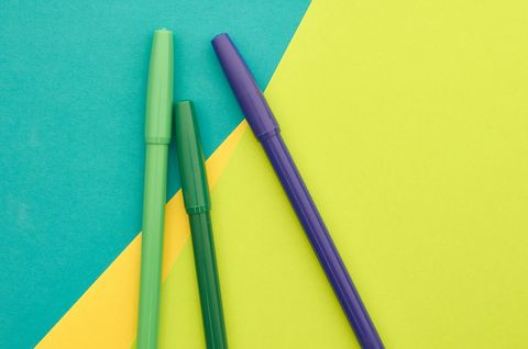 Bright green and purple markers lying on geometric teal, lime and yellow paper