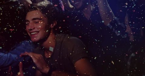 Smiling young man reaching through confetti at vibrant nightclub party