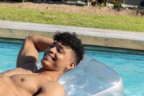 African american man reclining on clear inflatable float smiling in sunny backyard pool