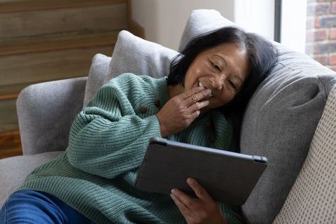 Senior Asian Woman Relaxing on Couch With Tablet in Cozy Living Room