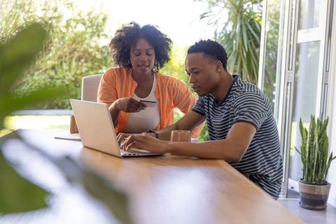 African american couple shopping online at home by glass doors using laptop and credit card