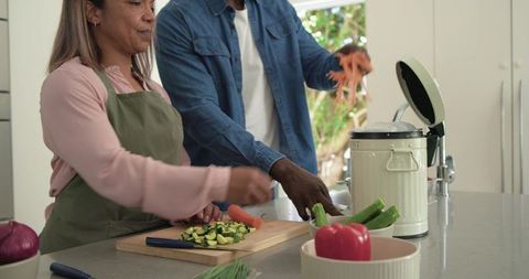 Mature couple preparing vegetables and composting scraps at home kitchen counter