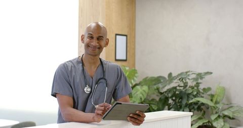 African male clinician holding tablet wearing gray scrubs and stethoscope in clinic