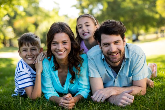 Family enjoying a sunny day in the park, lying on the grass and smiling. Perfect for advertisements, family-oriented campaigns, lifestyle blogs, and articles about family bonding and outdoor activities.