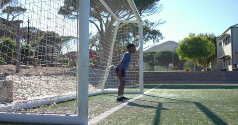 African youth goalkeeper standing alert in goal on sunlit soccer turf during training