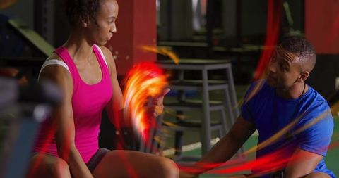 Female athlete holding kettlebell, trainer kneeling and coaching with dynamic light trails in gym