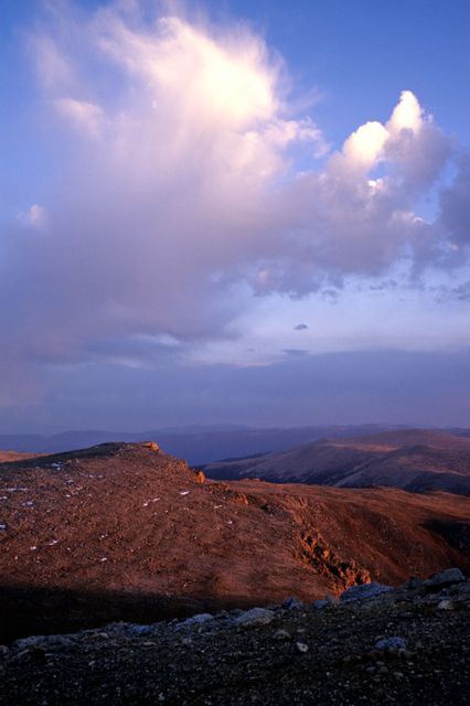 This nature scene shows a breathtaking view of a mountain range during sunset. Dramatic cloud formations float in the sky and the landscape is illuminated by soft evening light, creating a serene atmosphere. Ideal for use in travel brochures, nature magazines, desktop wallpapers, and backgrounds in presentations highlighting natural beauty.