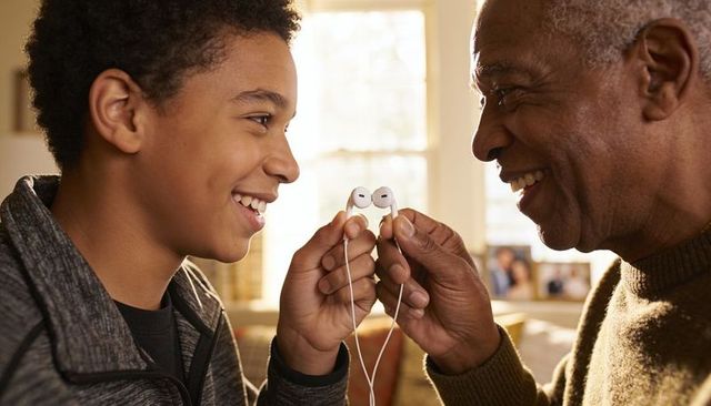 Grandfather and grandson sharing earbuds, smiling and bonding in warm family moment