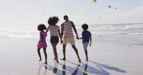 Black family walking on reflective wet sand with gold-star confetti at sunny beach