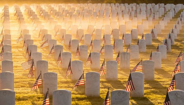 Sunrise glowing over military cemetery, rows of headstones and flags honoring veterans