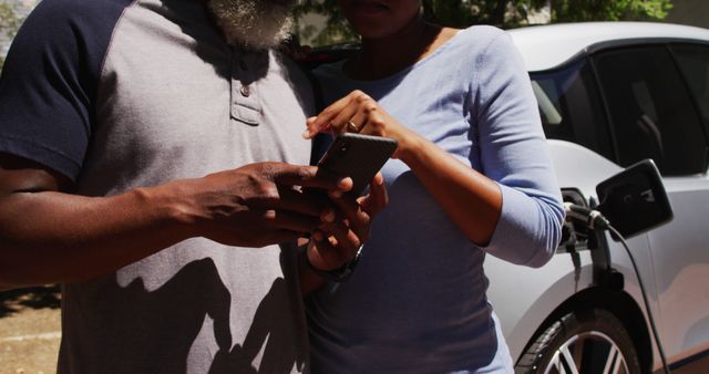Midsection of african american couple charging electric car and using smartphone on a sunny day - Download Free Stock Photos Pikwizard.com