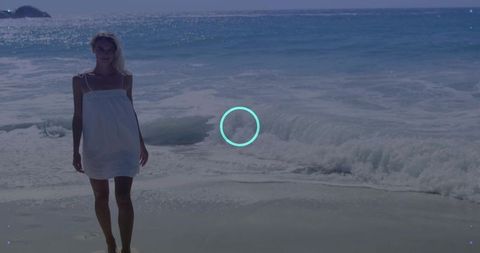 Woman standing on sunlit beach wearing white sundress, barefoot on wet sand, turquoise marker
