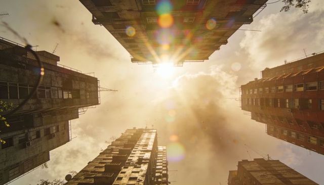 High-rise towers converging toward sun in golden hour urban canyon with cinematic lens flare