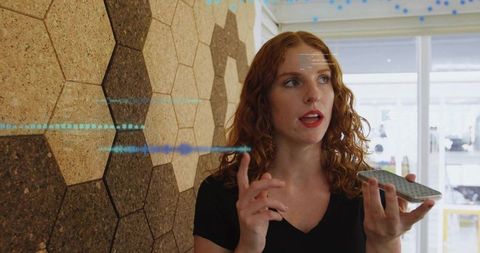 Redhead woman holding smartphone speaking with voice waveform overlay in modern office